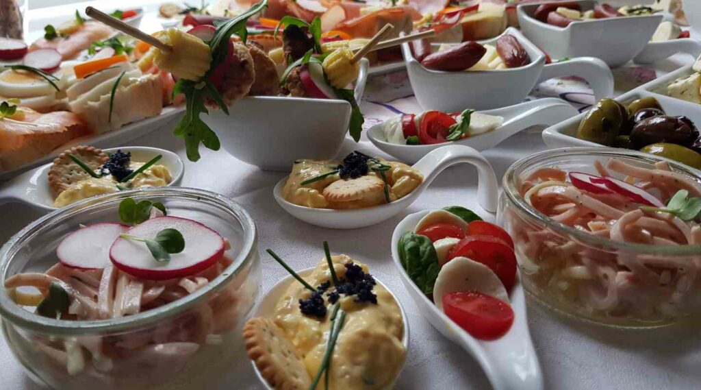 Fingerfood-Buffet mit kleinen Häppchen, Salaten und Gemüse in Gläsern und Schälchen.