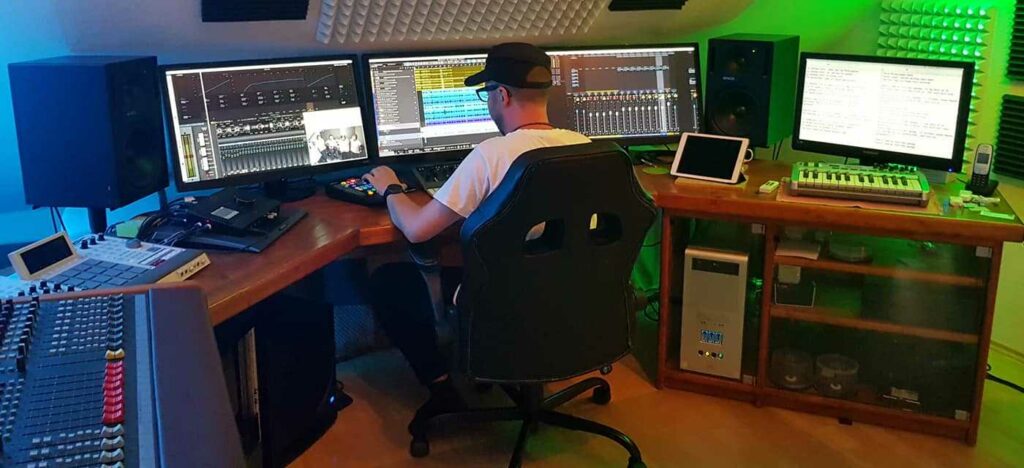 Eine Person sitzt am Studio-Arbeitsplatz vor mehreren Bildschirmen mit Audiosoftware.